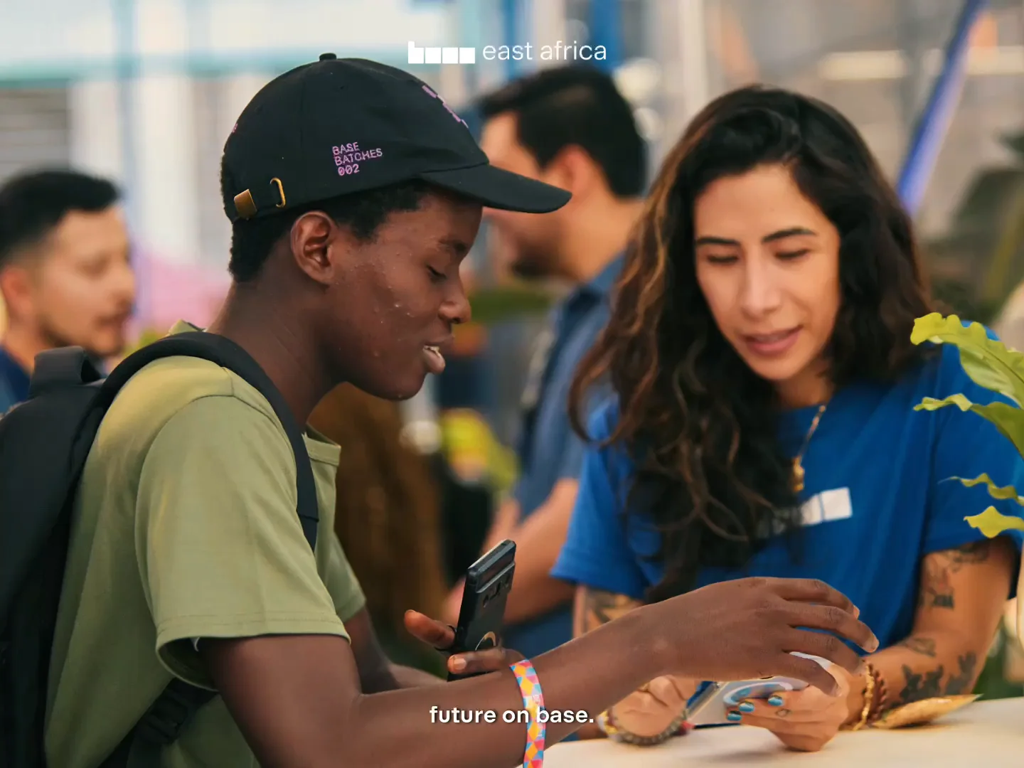 Still from the Base Batches 003 film: a participant in a Base Batches cap talking with a Base team member at an event