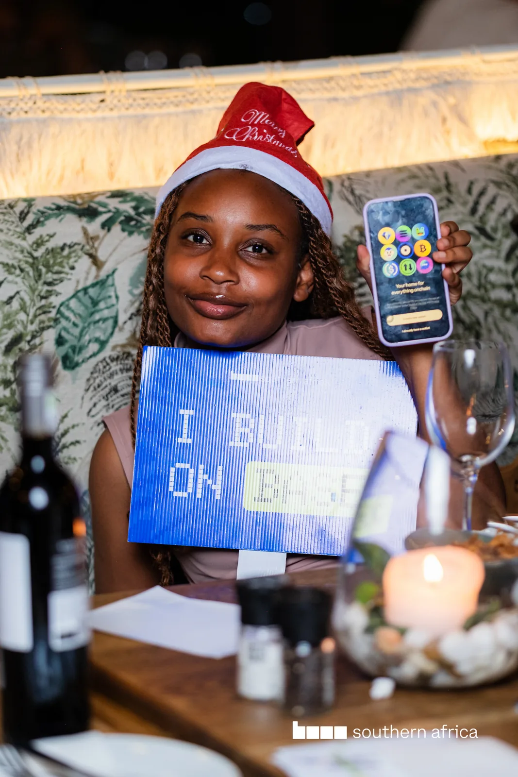 An attendee holding an “I build on Base” card and a phone at a Base event
