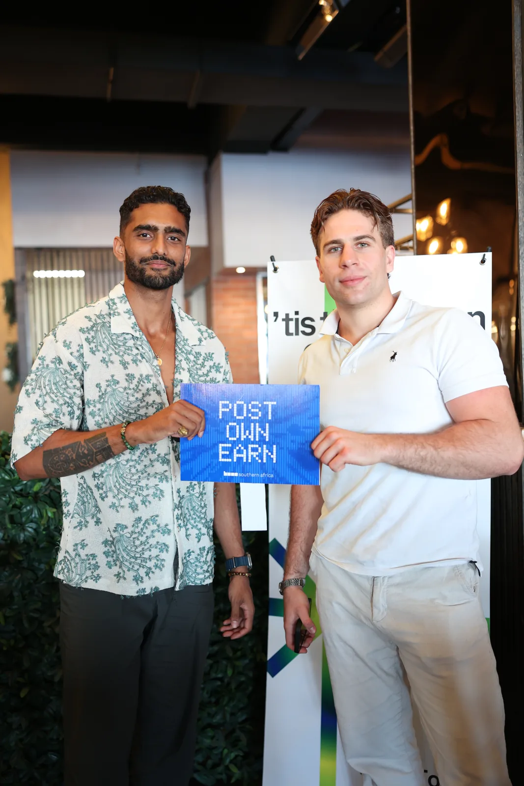 Two people at a Base event holding “Post. Own. Earn.” campaign cards